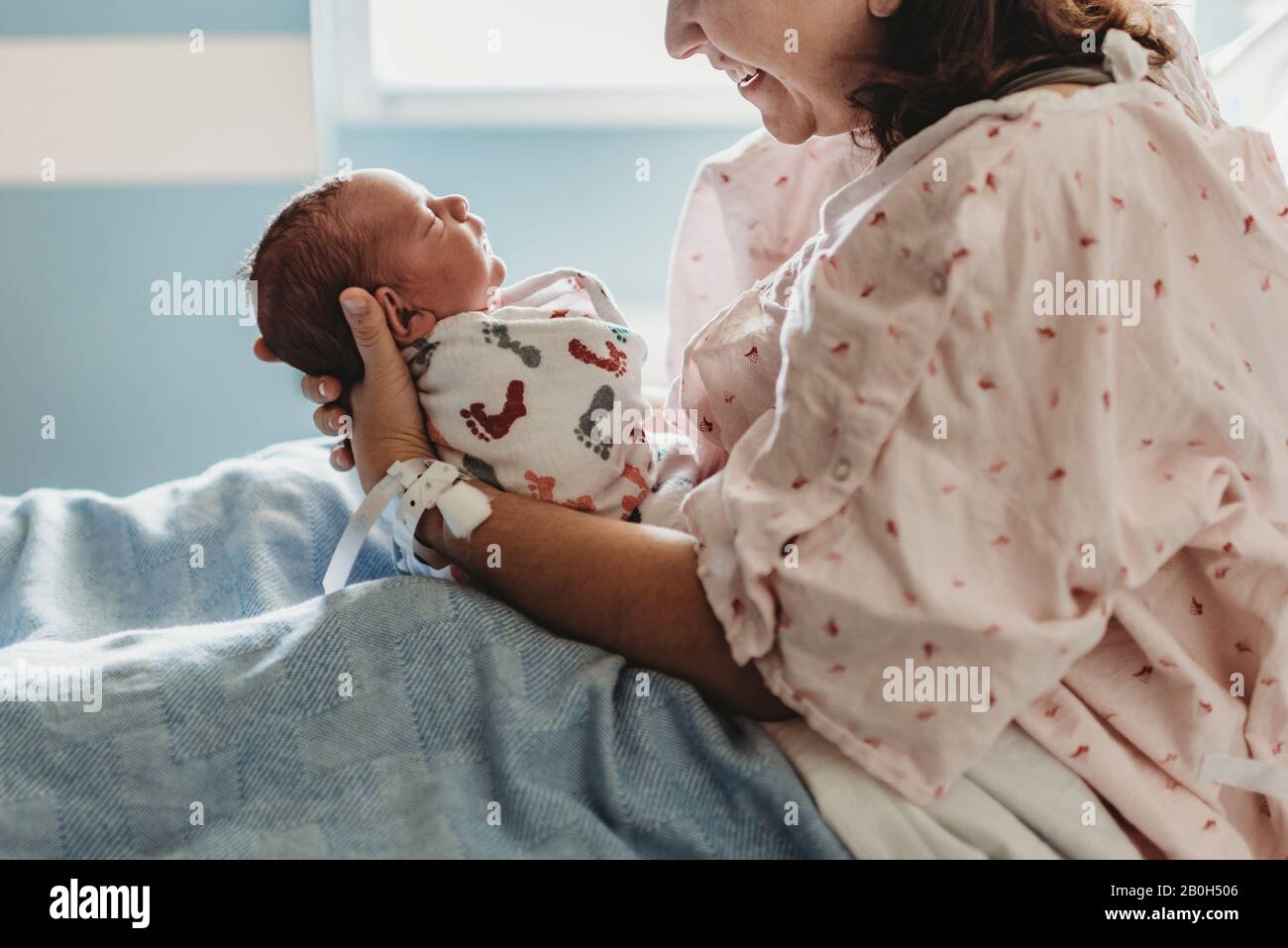Vista laterale della madre che guarda e sorride al neonato figlio in ospedale Foto Stock