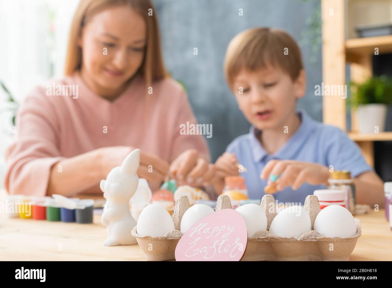 Tradizione di famiglia prima di Pasqua: Focus sulle uova in cartone e carta di Pasqua rosa, madre e figlio pittura uova in background Foto Stock