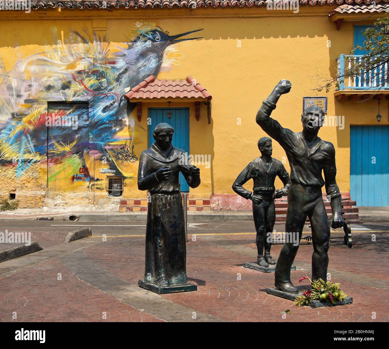 Sculture di eroi indipendenti in Plaza Trinidad di fronte all'arte di strada che decorano un edificio coloniale a Getsemani, Cartagena, Colombia Foto Stock