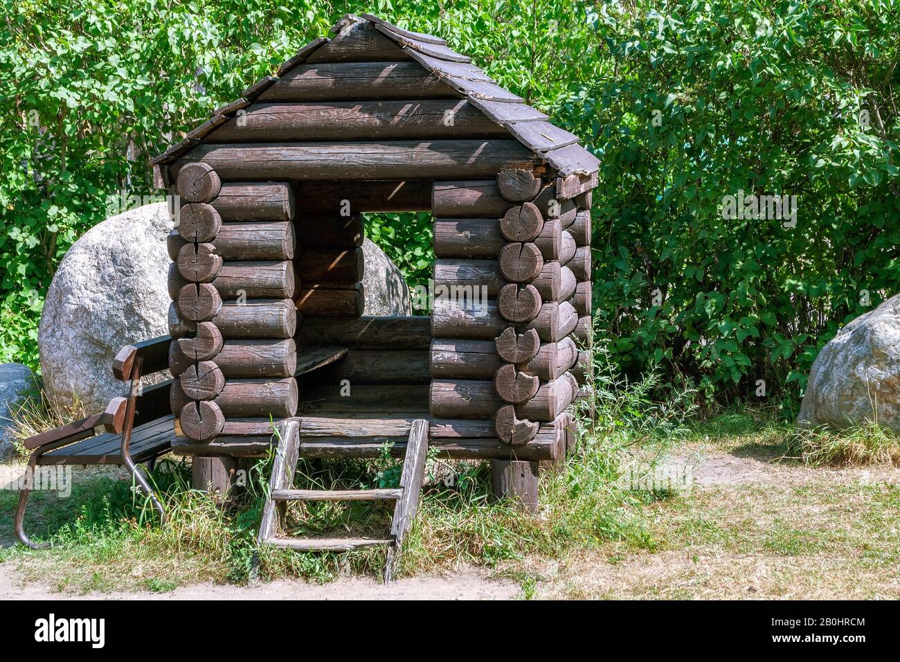 Piccola casa di tronchi di legno tra pietre e cespugli verdi. Foto Stock