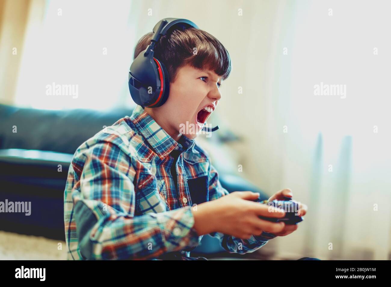 Pazzo dipendente capretto gridando durante il gioco di massa multiplayer video gioco online a casa Foto Stock