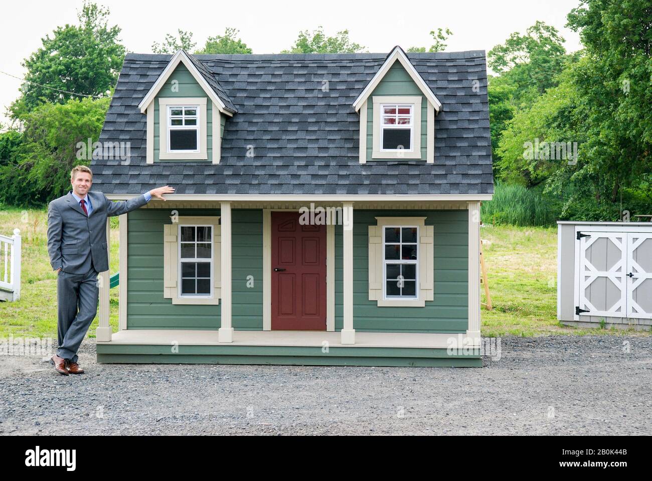 Fiero uomo d'affari che sta all'aperto vicino ad una piccola casa verde Foto Stock