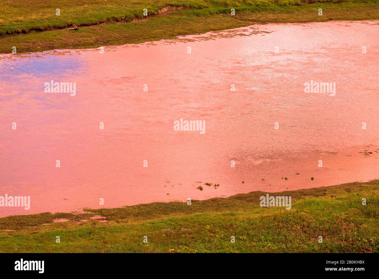 Verdi rive del fiume con il fiume che riflette il cielo rosso arancio. Foto Stock