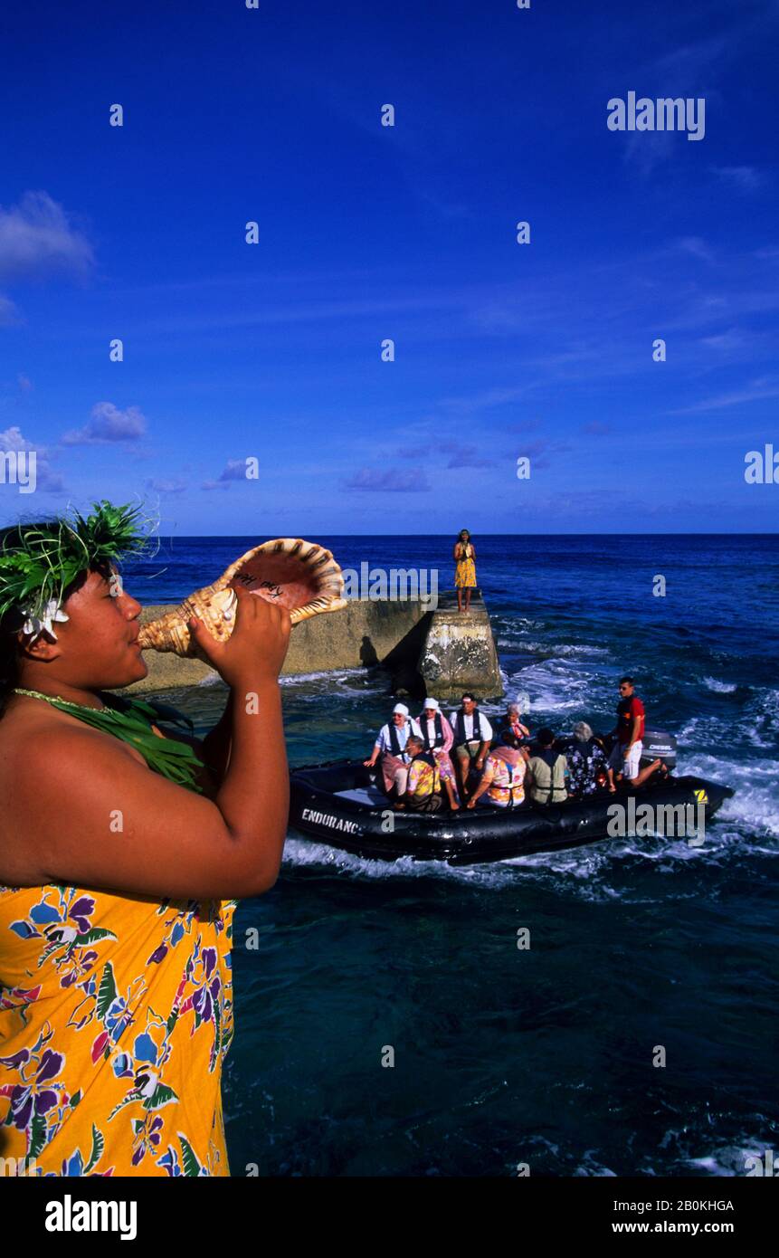 ISOLE COOK, ISOLA DI ATIU, RAGAZZA CHE SOFFIA IN SEASHELL (CORNO), SALUTARE I TURISTI A ZODIAC Foto Stock