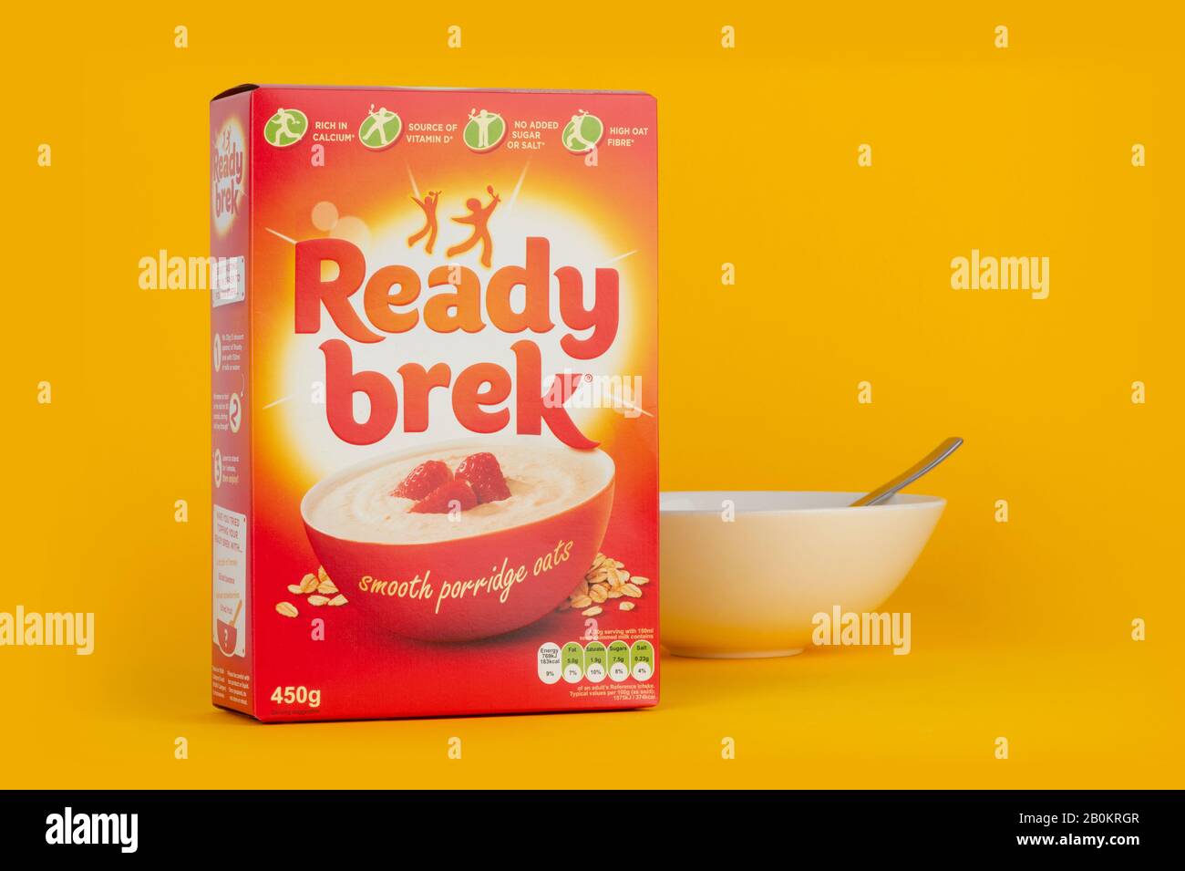 Una scatola di cereali pronti da latte sparato su uno sfondo giallo con una ciotola per la colazione e un cucchiaio. Foto Stock