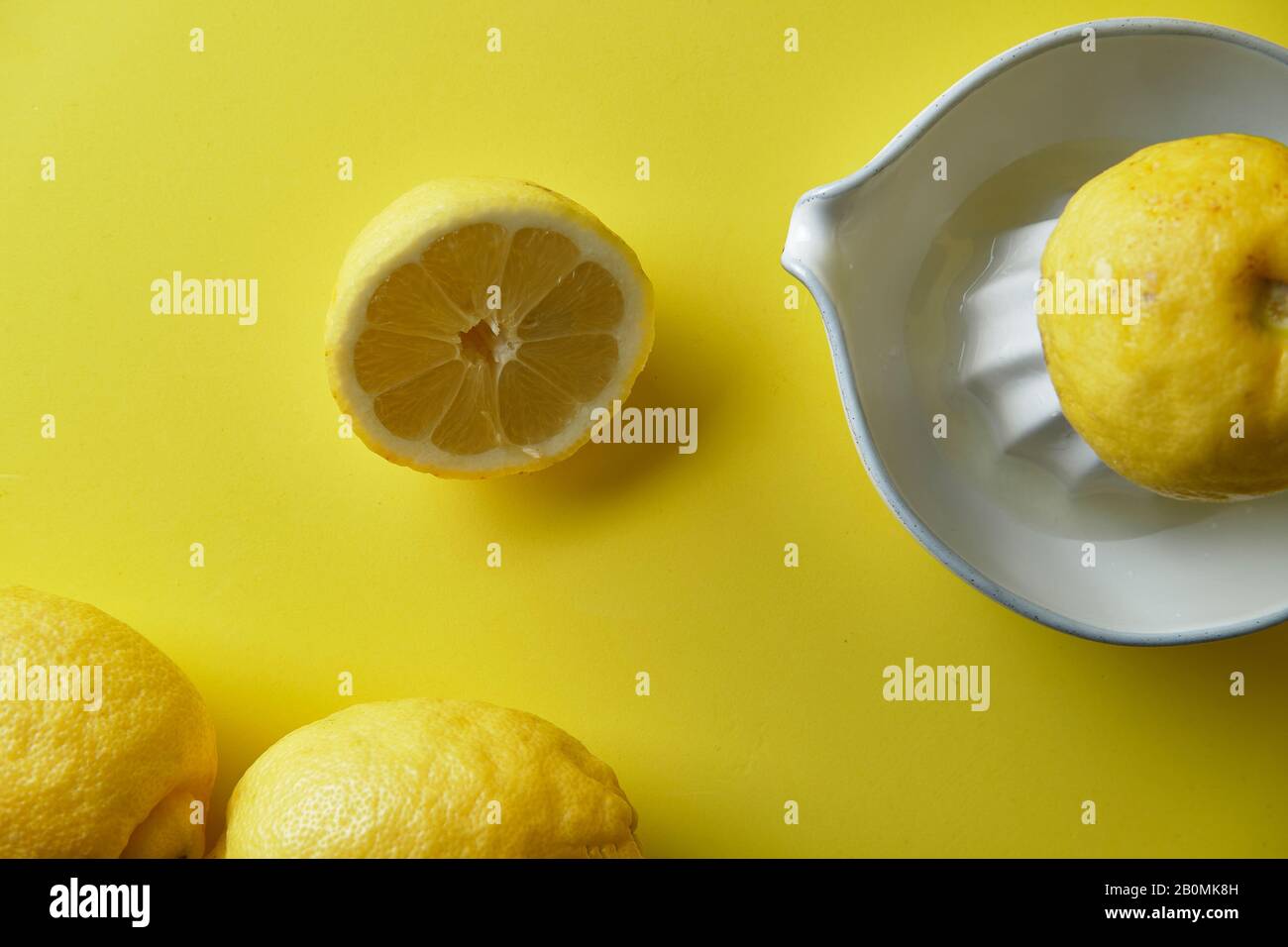 spremitura di un limone in una centrifuga bianca in ceramica su sfondo giallo Foto Stock