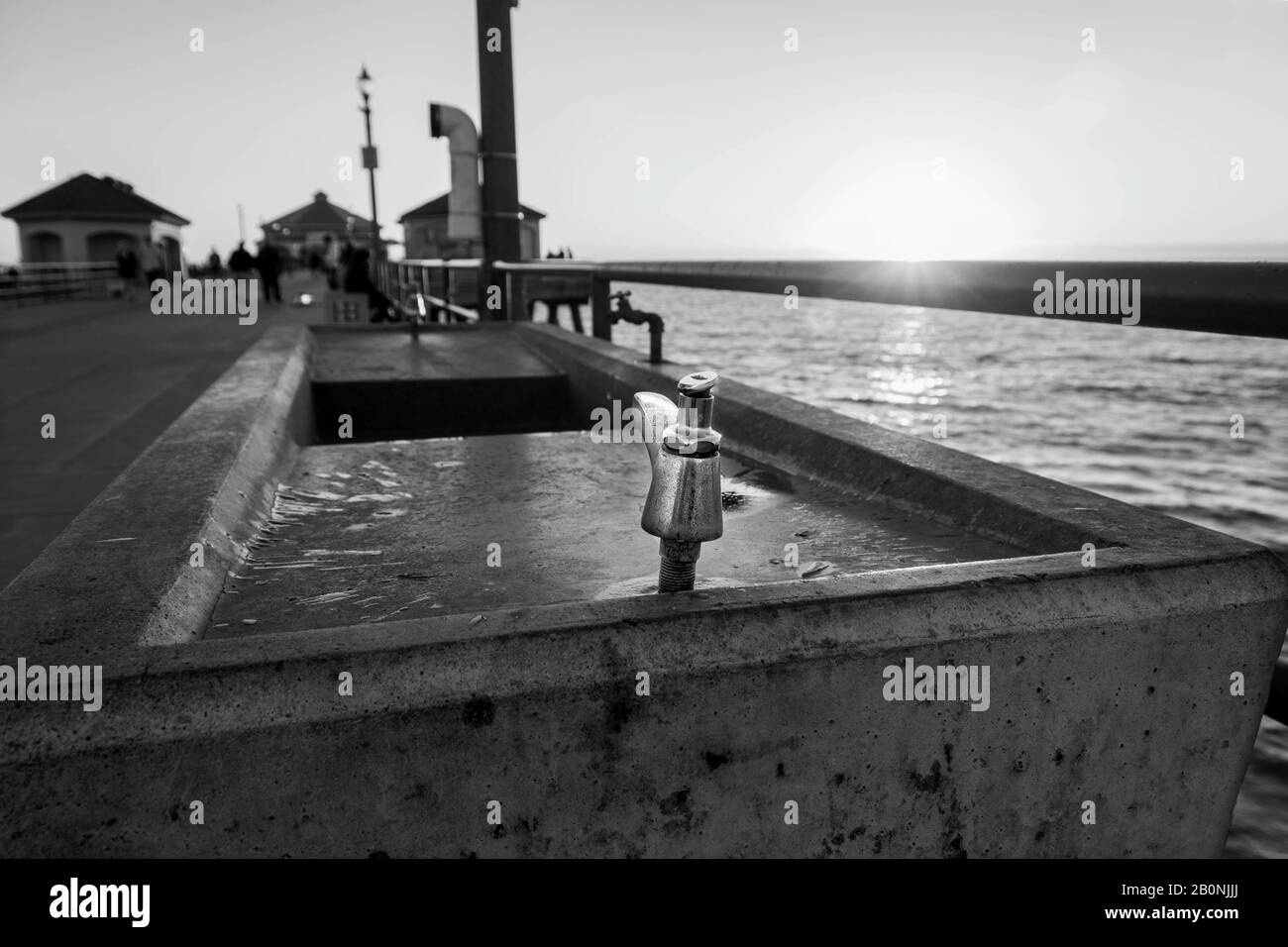 Primo piano di una fontana pubblica in acciaio inossidabile e cemento sul molo di Huntington Beach al tramonto. Raggi solari all'orizzonte. Foto Stock