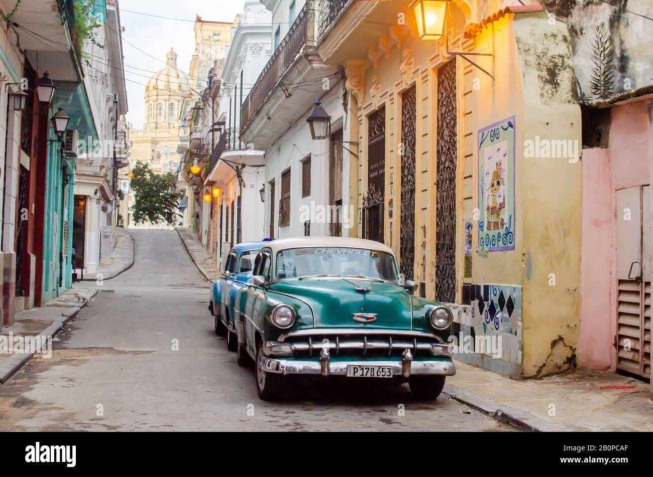 La mattina presto nelle strade dell'Avana Vecchia. Due auto classiche sono viste sulla sinistra e il Museo della Rivoluzione è visto in lontananza Foto Stock