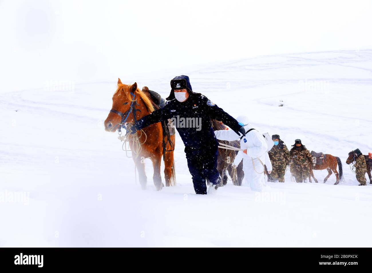 Funzionari di polizia, guardie di frontiera e medici cinesi camminano con cavalli nella neve per visitare le famiglie locali per la prevenzione del nuovo coronavirus Foto Stock