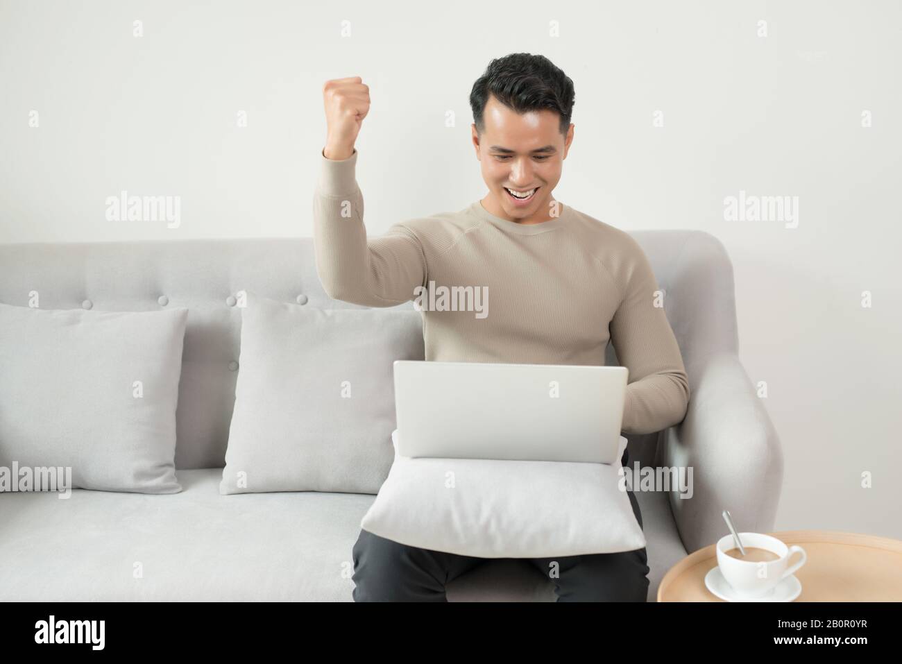 Felice giovane uomo usando il suo computer portatile nel salotto luminoso. Foto Stock