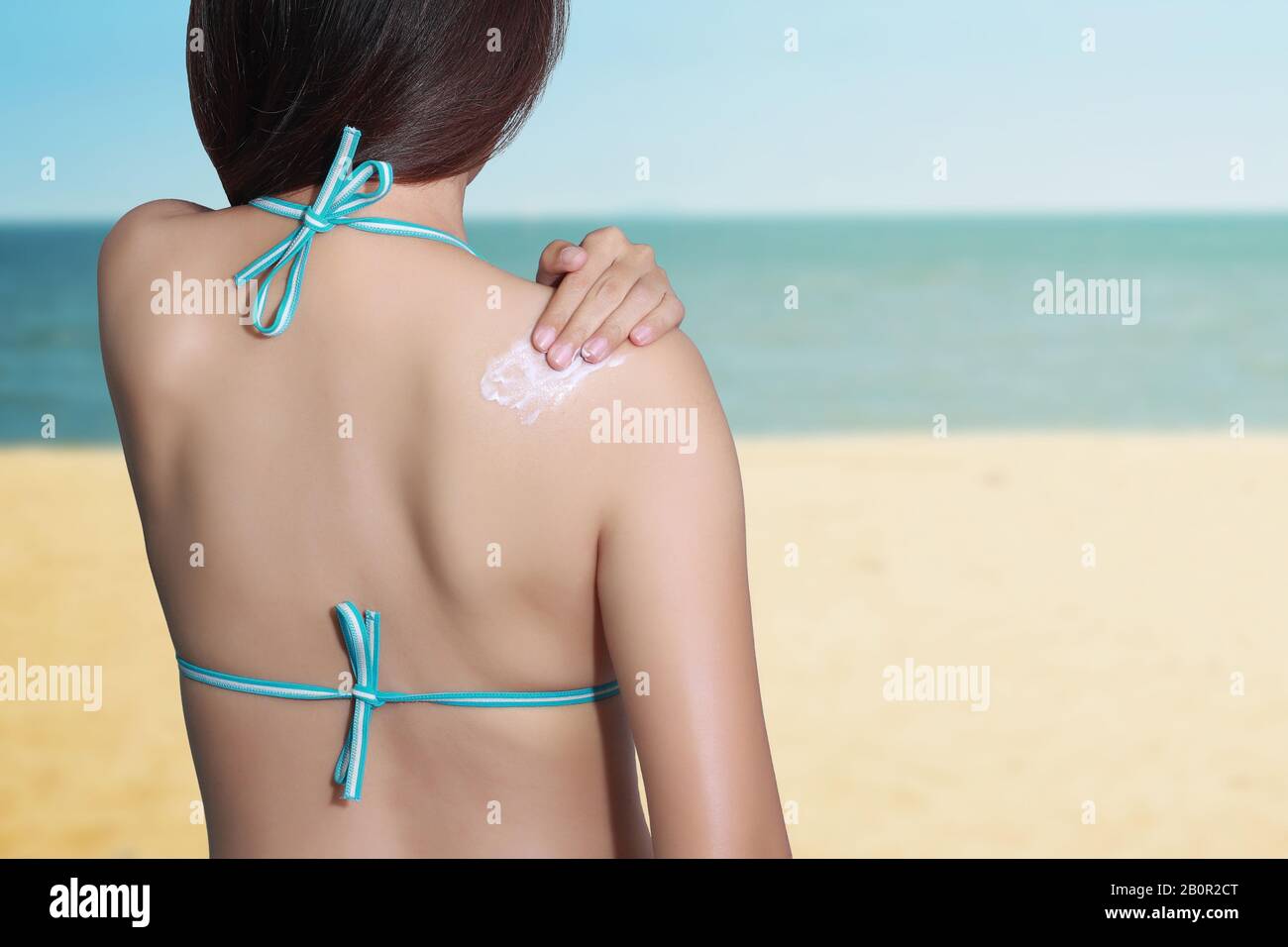 donna che applica la protezione solare sulla sua schiena con sfondo mare. Concetto di protezione del blocco solare SPF. Vacanze di viaggio Foto Stock