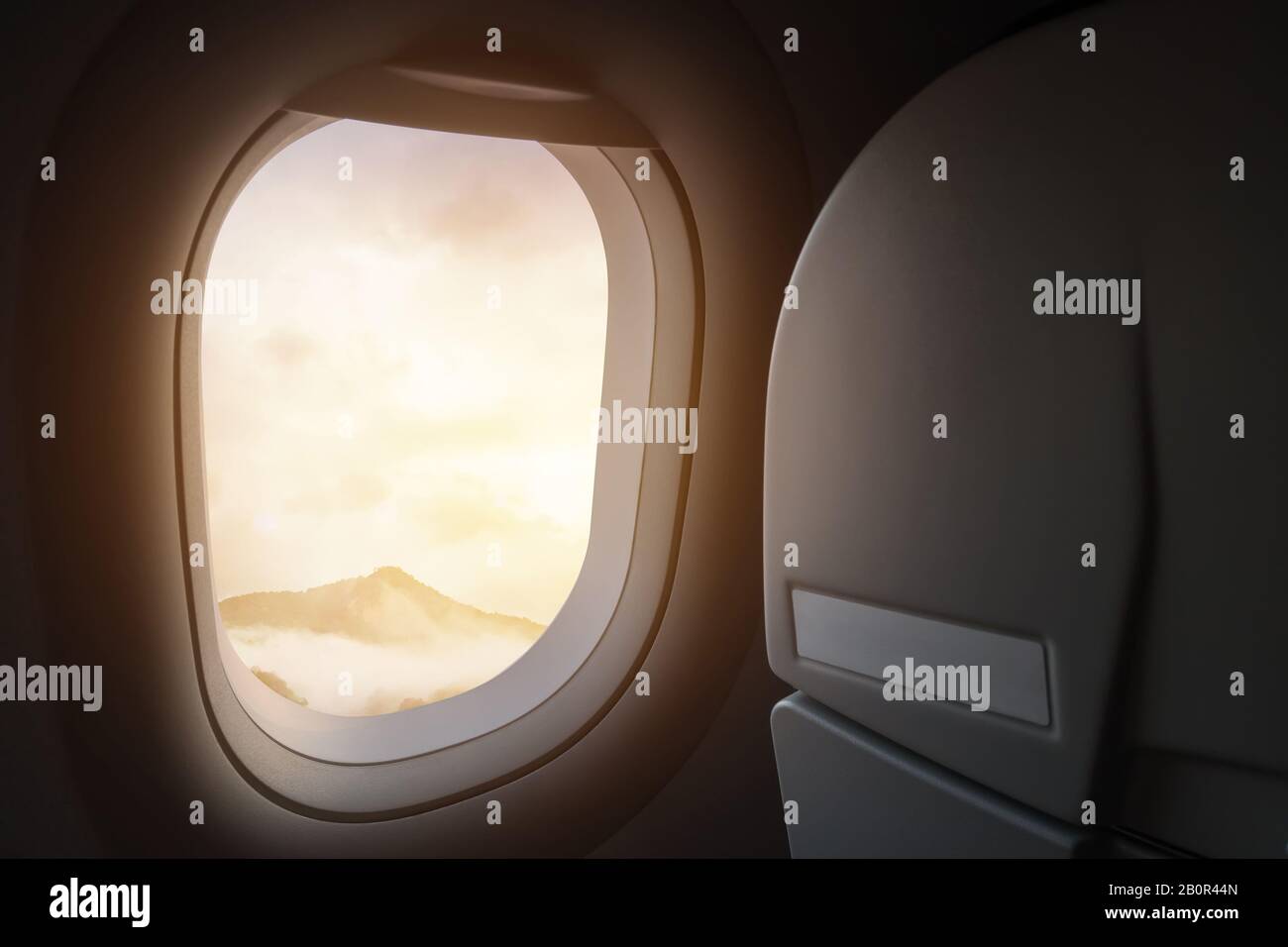 viaggio e viaggio in aereo. vista della splendida montagna e nebbia con luce solare dorata e bagliore lente come si vede attraverso la finestra di un aereo Foto Stock