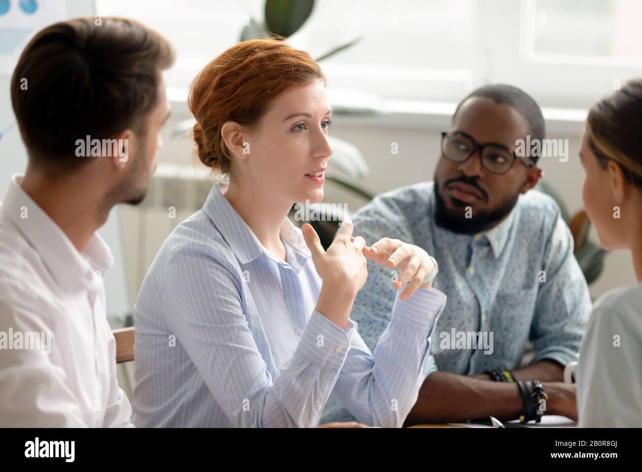 Donna d'affari sicura, coach discutere progetto con diversi colleghi al briefing in sala riunioni, condividere pensieri, idee, dipendenti con attenzione lis Foto Stock