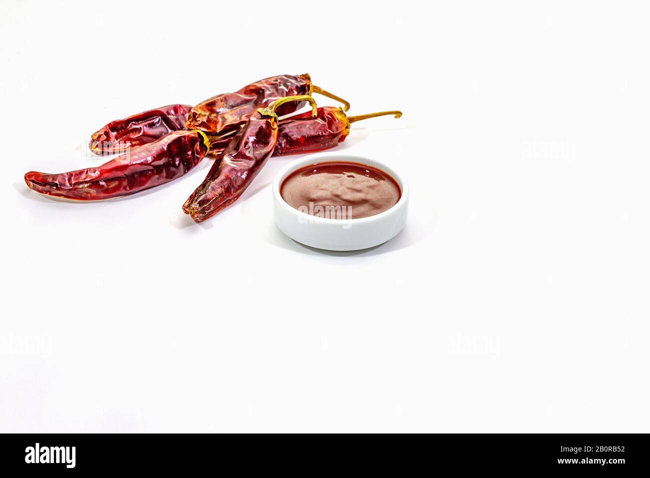 Salsa piccante al peperoncino in ciotola isolata su fondo bianco. Diverse varietà di peperoni caldi secchi, ingrediente principale per la preparazione. Sfondo cucina, moc Foto Stock