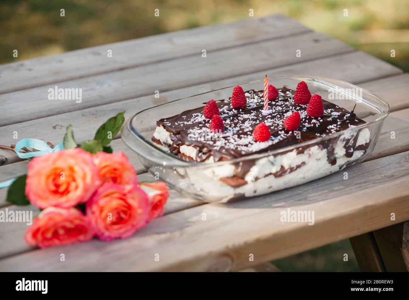 torta di compleanno al cioccolato fatta in casa con frutti di bosco freschi e una candela e rose Foto Stock