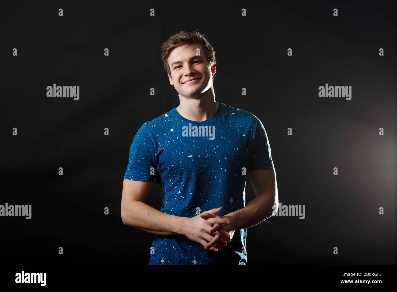 Un giovane uomo in t-shirt blu con le stelle stampa in piedi nella sua fronte e sorridente con sfondo scuro Foto Stock