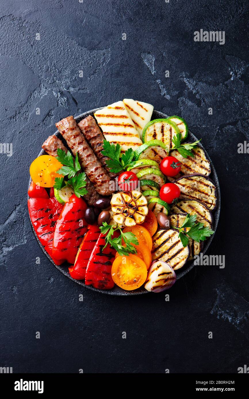 Spiedini e verdure di carne alla griglia su un piatto nero. Sfondo in pietra nera. Vista dall'alto. Foto Stock