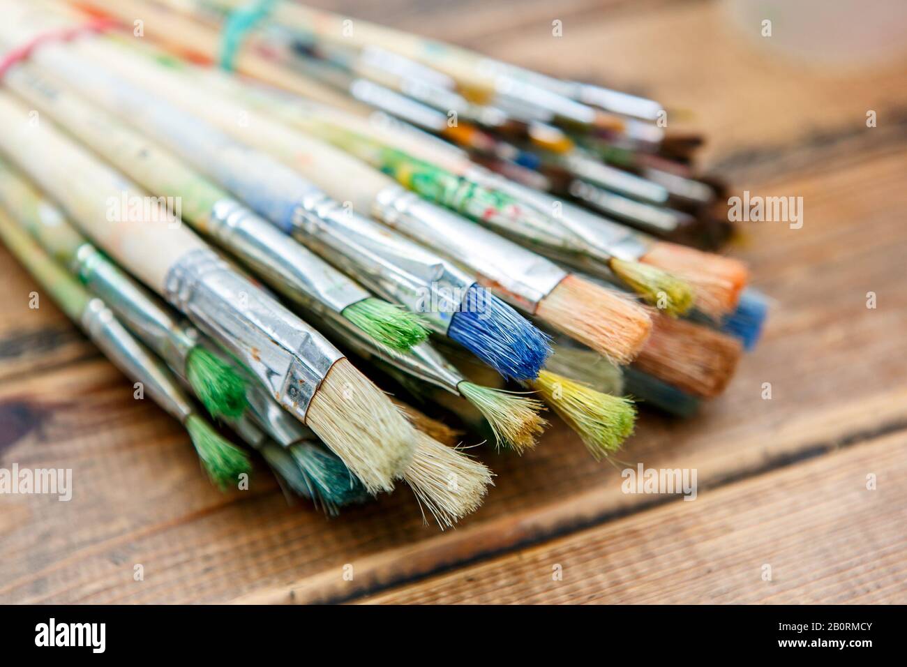 Un primo piano dei pochi pennelli con tracce di vernice su di essi sul tavolo di legno Foto Stock