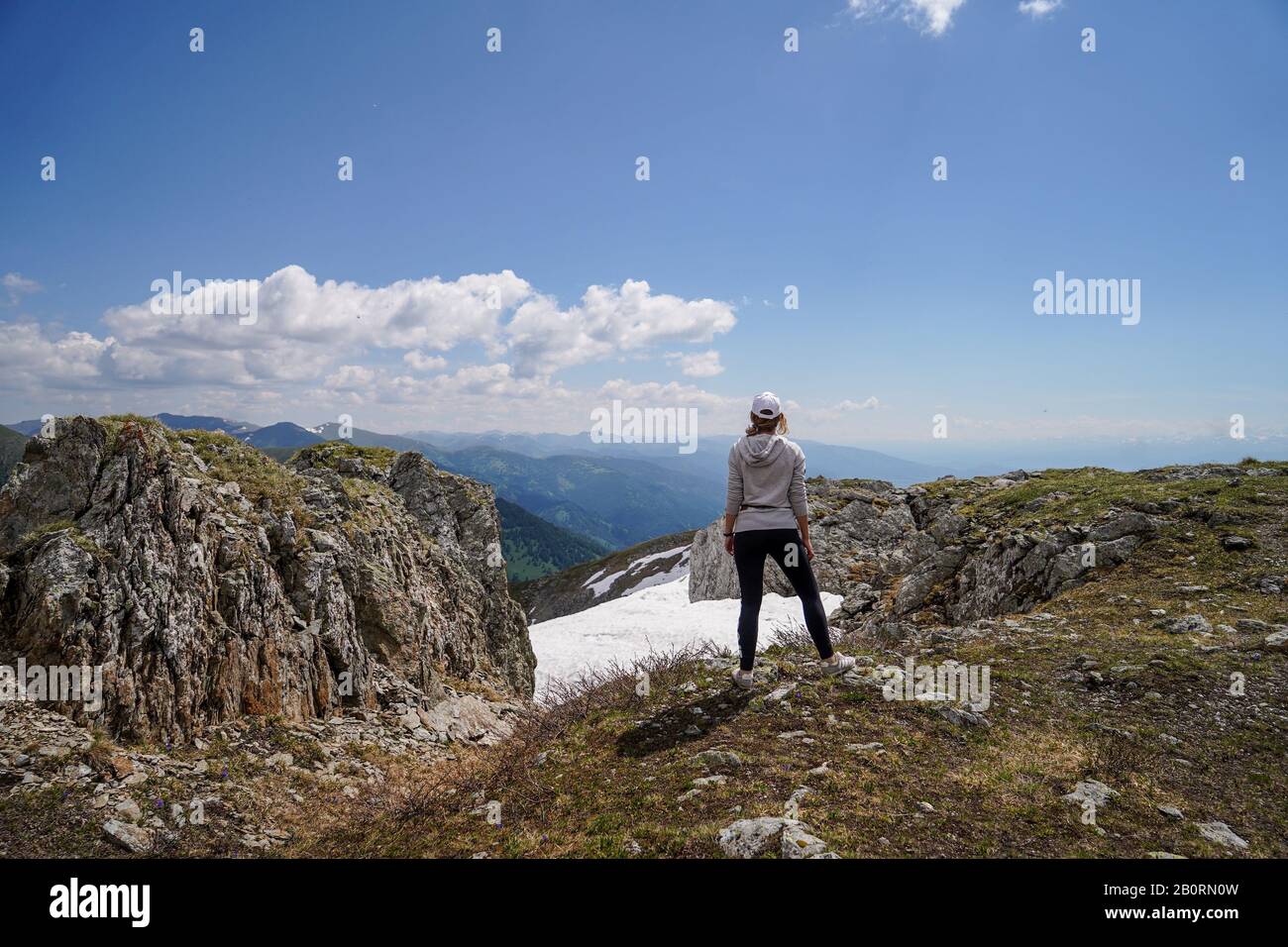 Una donna in grigio hoody in piedi girare la schiena su rocce di fronte al cielo sfondo Foto Stock