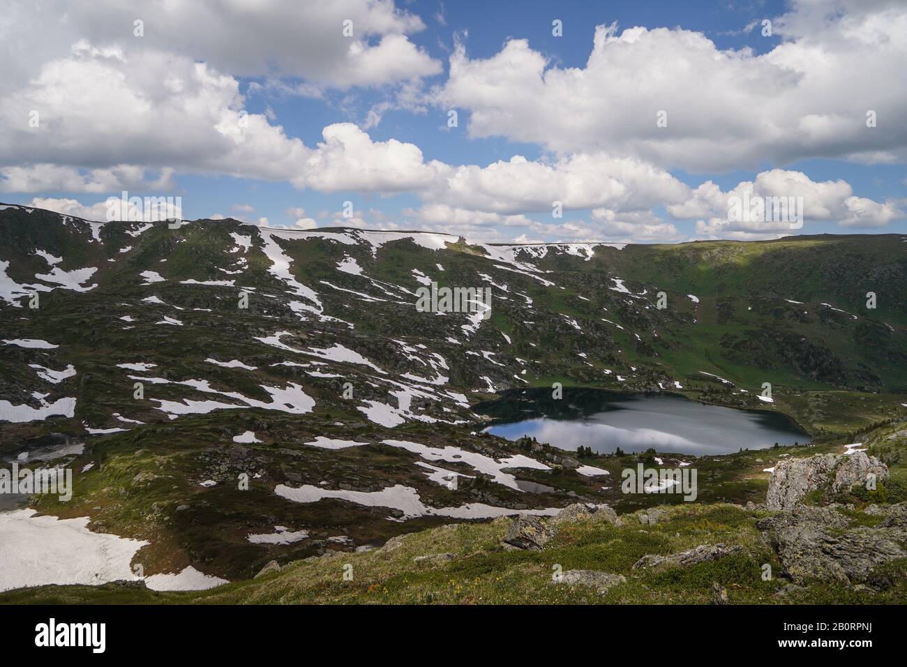 Piccolo lago nella valle di montagna e piccole banche di neve che vi circondano Foto Stock