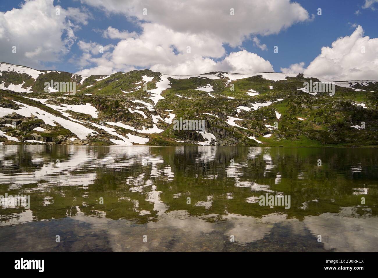 Piccolo lago di montagna circondato da piste di montagna coperte con piccole snowbanks Foto Stock