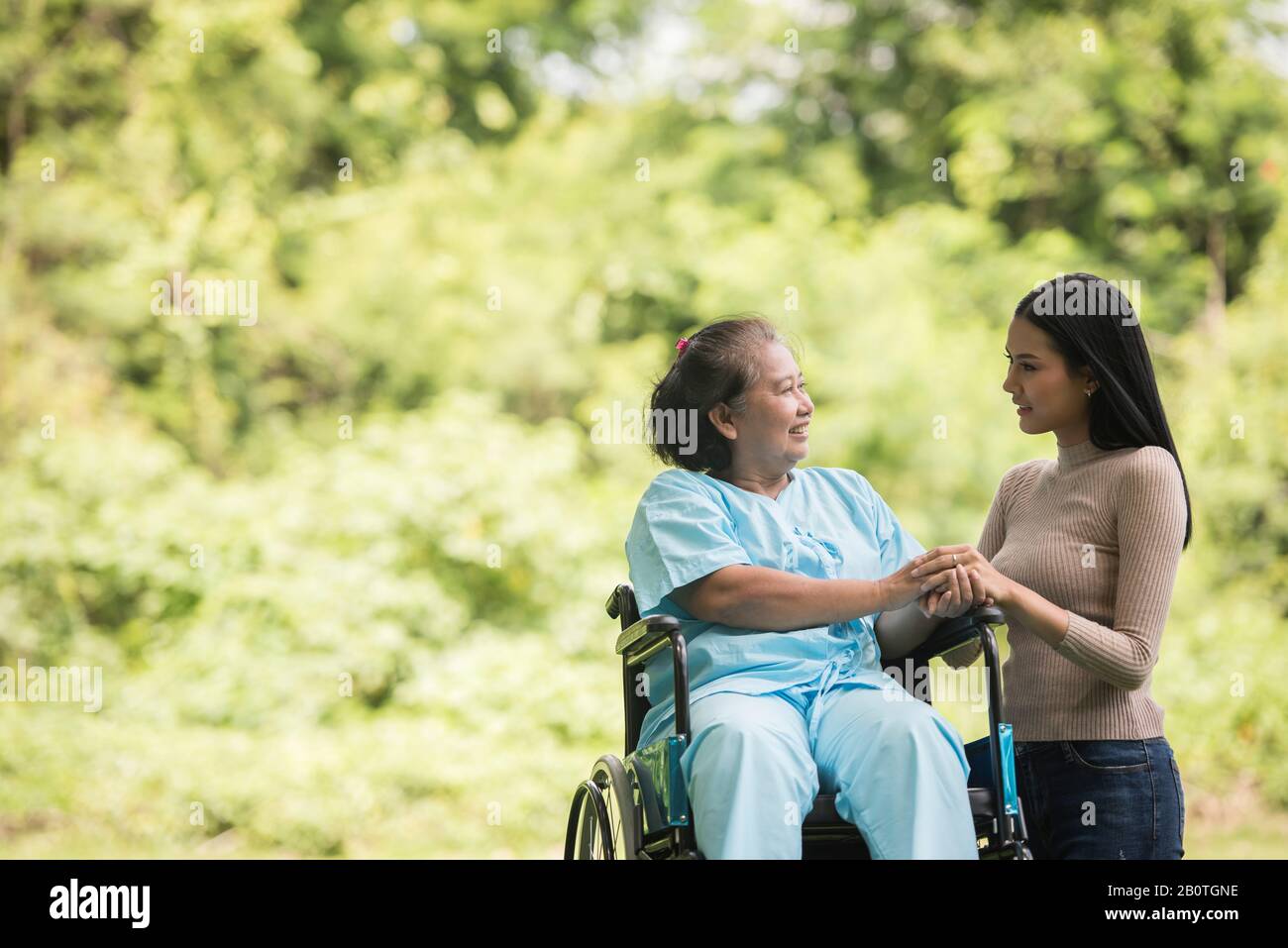 Nipote che parla con la nonna seduta su sedia a rotelle, concetto allegro, famiglia felice Foto Stock