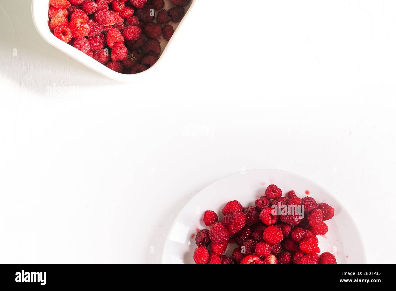 Piatto e contenitore con lamponi su fondo bianco. Lamponi freschi sul tavolo con spazio copia. Layout piatto, vista dall'alto Foto Stock