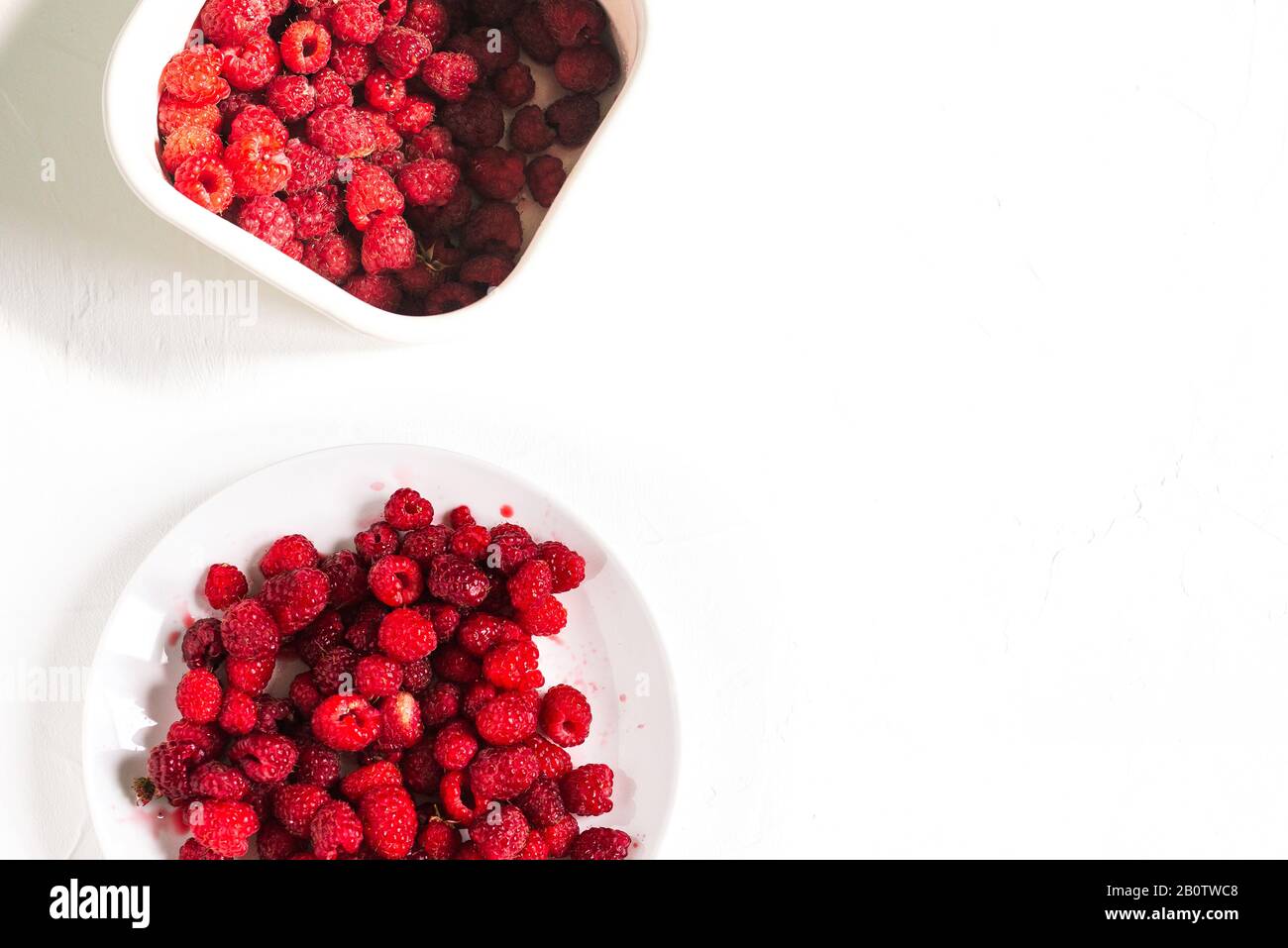 Piatto e contenitore con lamponi su fondo bianco. Lamponi freschi sul tavolo con spazio copia. Layout piatto, vista dall'alto Foto Stock