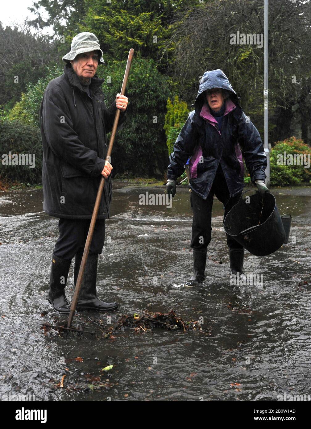 Kilbarchan, Scozia, Regno Unito. 21th febbraio 2020. I residenti cercano di deviare l'acqua allagando la propria strada sbloccando gli scarichi. Foto Stock