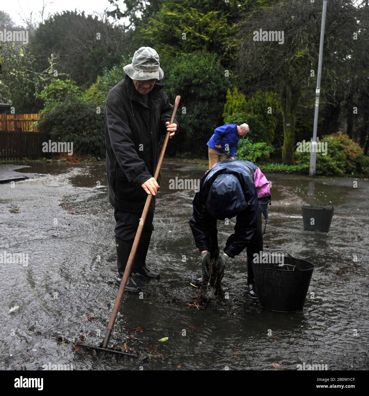 Kilbarchan, Scozia, Regno Unito. 21th febbraio 2020. I residenti cercano di deviare l'acqua allagando la propria strada sbloccando gli scarichi. Foto Stock