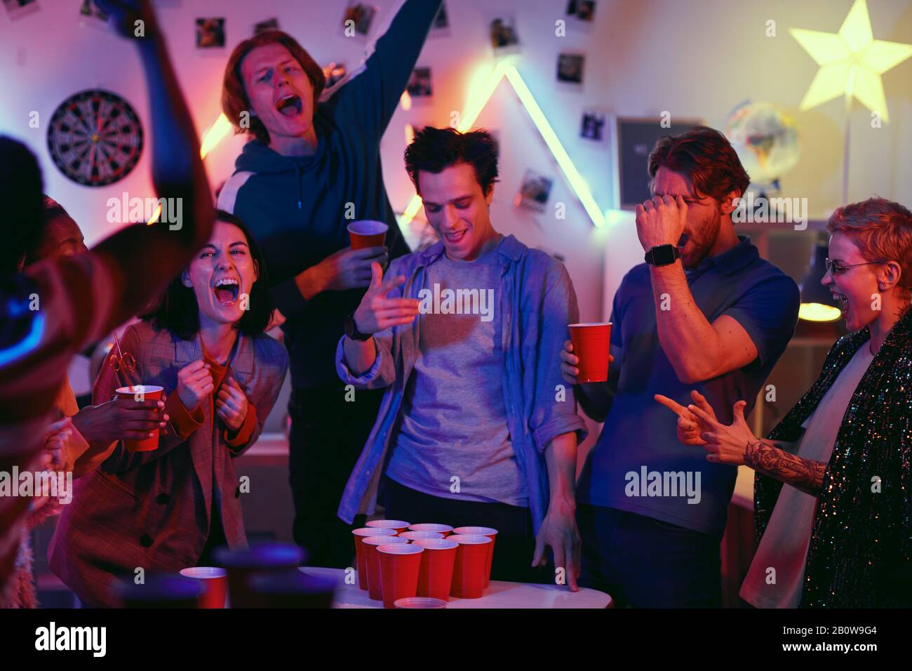 I giovani eccitati bevono birra e giocano a beer pong durante la festa di casa Foto Stock