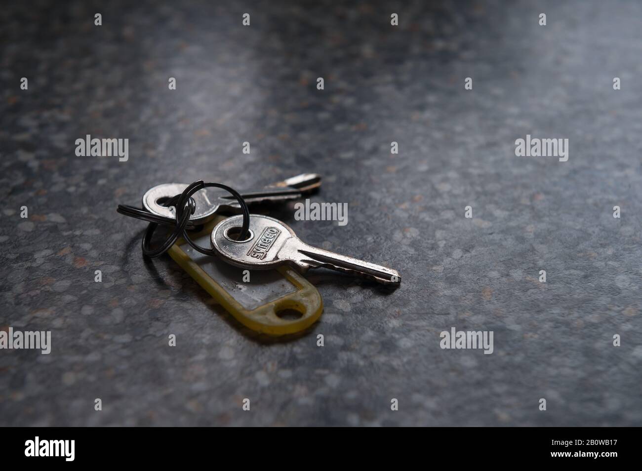 Set o mazzo di tre chiavi lasciate sul banco della superficie di lavoro con etichetta di identità gialla sul piano di lavoro Foto Stock