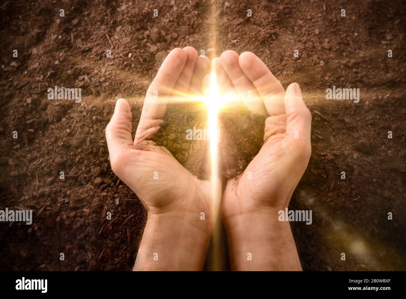 Mani insieme con un piccolo tumulo di terra con un flash dorato a forma di croce su uno sfondo di terra. Concetto di risurrezione di Gesù. Orizzontale Foto Stock