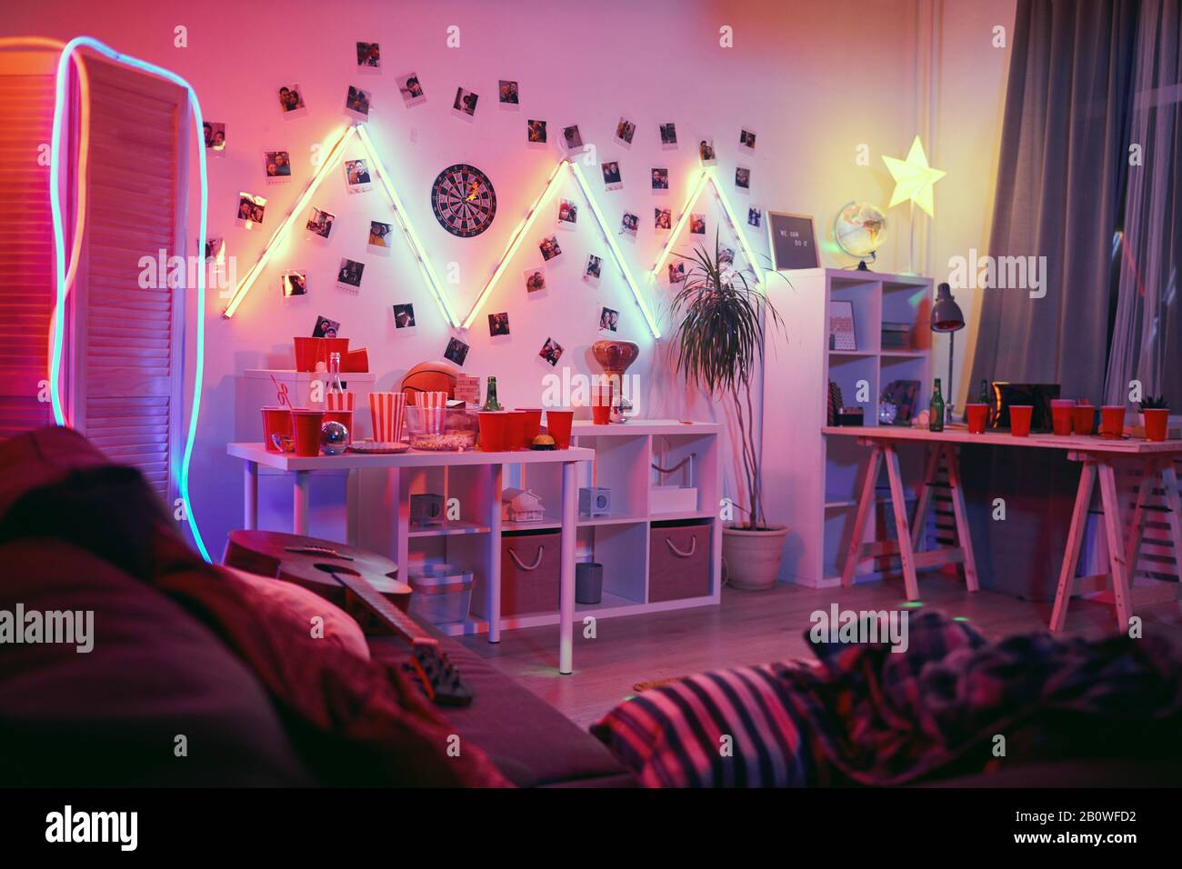 Immagine della sala interna decorata con luci e bicchieri vuoti per bevande e bottiglie vuote sul tavolo la festa è finita Foto Stock