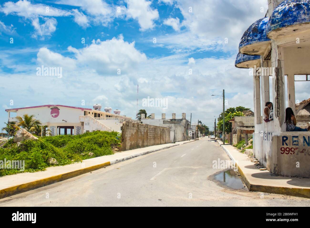 Strada del villaggio sul mare sotto il cielo blu con soffici nuvole con acqua in piedi, biciclo in strada e donne seduti in padiglione a lato Yucatan M. Foto Stock