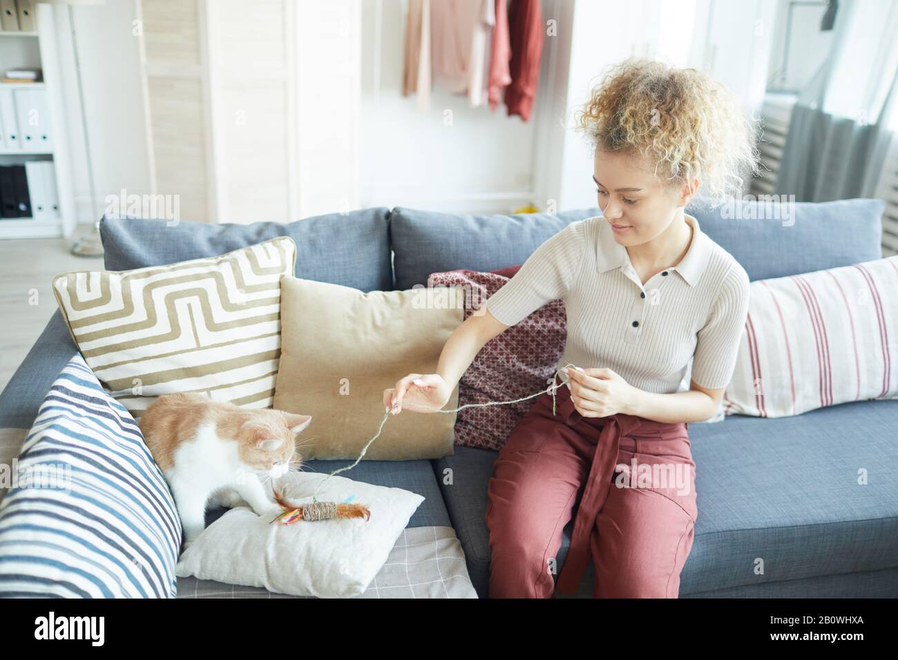 Giovane donna seduto sul divano e giocando con il suo gatto domestico nel soggiorno a casa Foto Stock