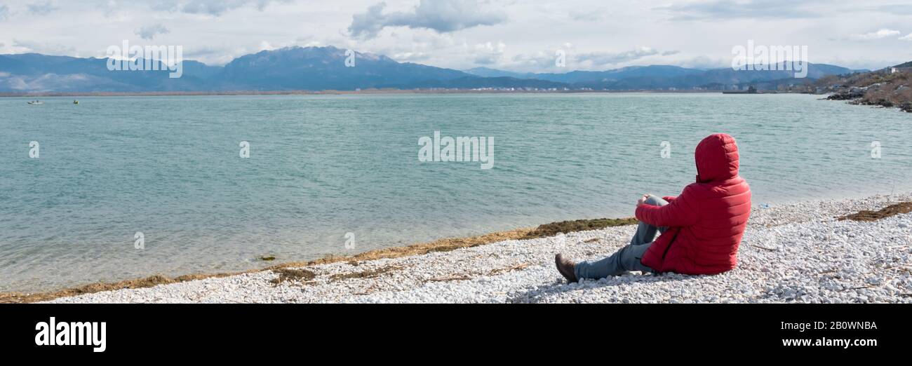 Uomo solitario seduto sul lungolago, ammirando la natura. Persona irriconoscibile, wanderlust Foto Stock