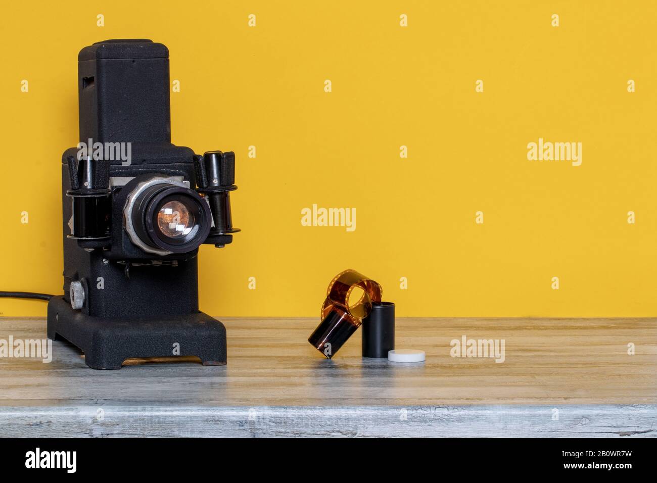 Primo piano di un vecchio proiettore nero in funzione per visualizzare diapositive e filmstripe e un film a colori negativo sul tavolo su sfondo giallo. Intrattenimento Foto Stock