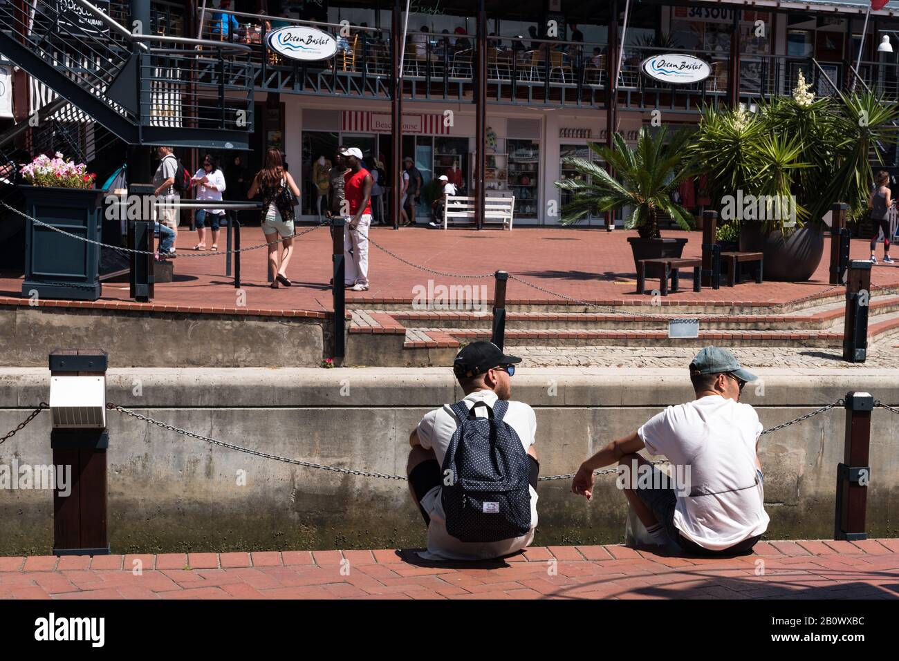 Mossel Bay, Sud Africa -- 9 gennaio 2018 -- Due giovani uomini seduti accanto ai moli di un centro commerciale. Foto Stock