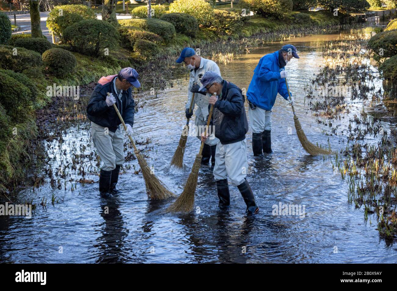 Lavoratori pulizia fiume con spazzole, Kenroku-en Garden, Kanazawa, Giappone Foto Stock