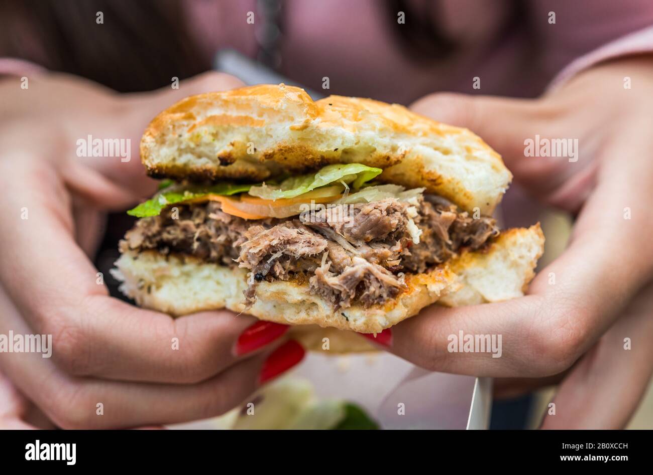 Giovane donna che mangia un hamburger di carne di anatra in un mercato alimentare di strada. Foto Stock