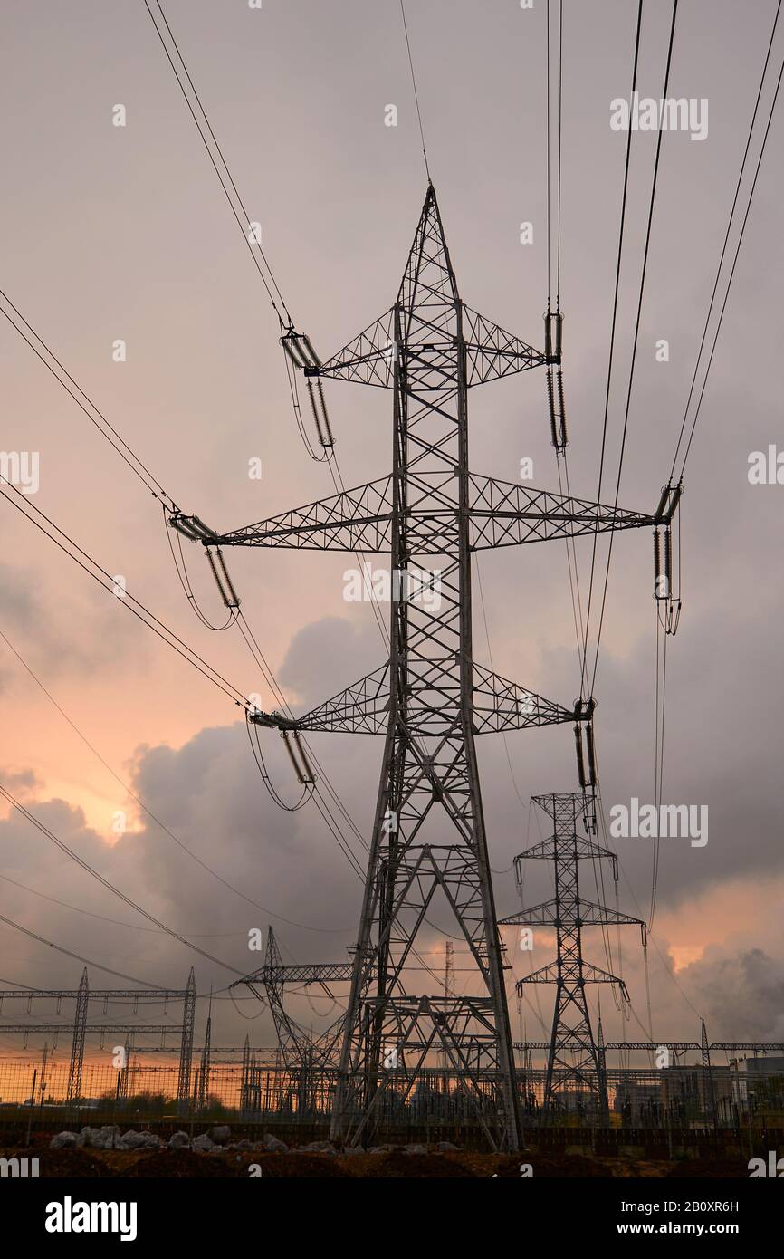 La silhouette della torre di trasmissione e le linee di trasmissione sopraelevate ad alta tensione, al tramonto, con cieli arancioni e nuvole tempestose. Foto Stock
