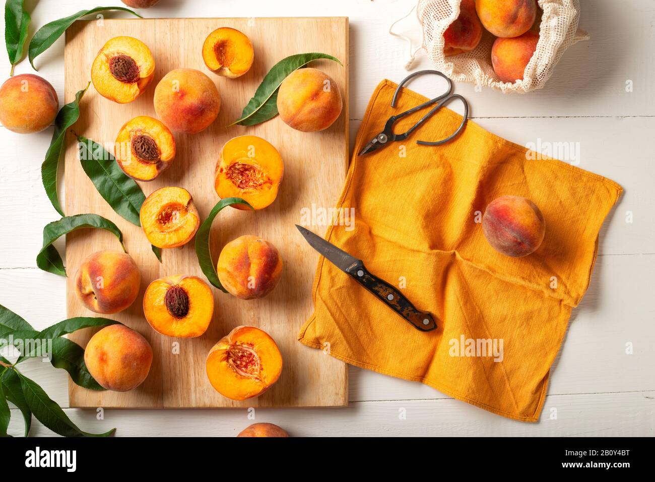 Pesche frutta intera con foglie, pesche a metà, fette di pesca su un tavolo da cucina bianco. Il processo di preparazione di confettura di pesche, cucinare dolce di pesca su Foto Stock