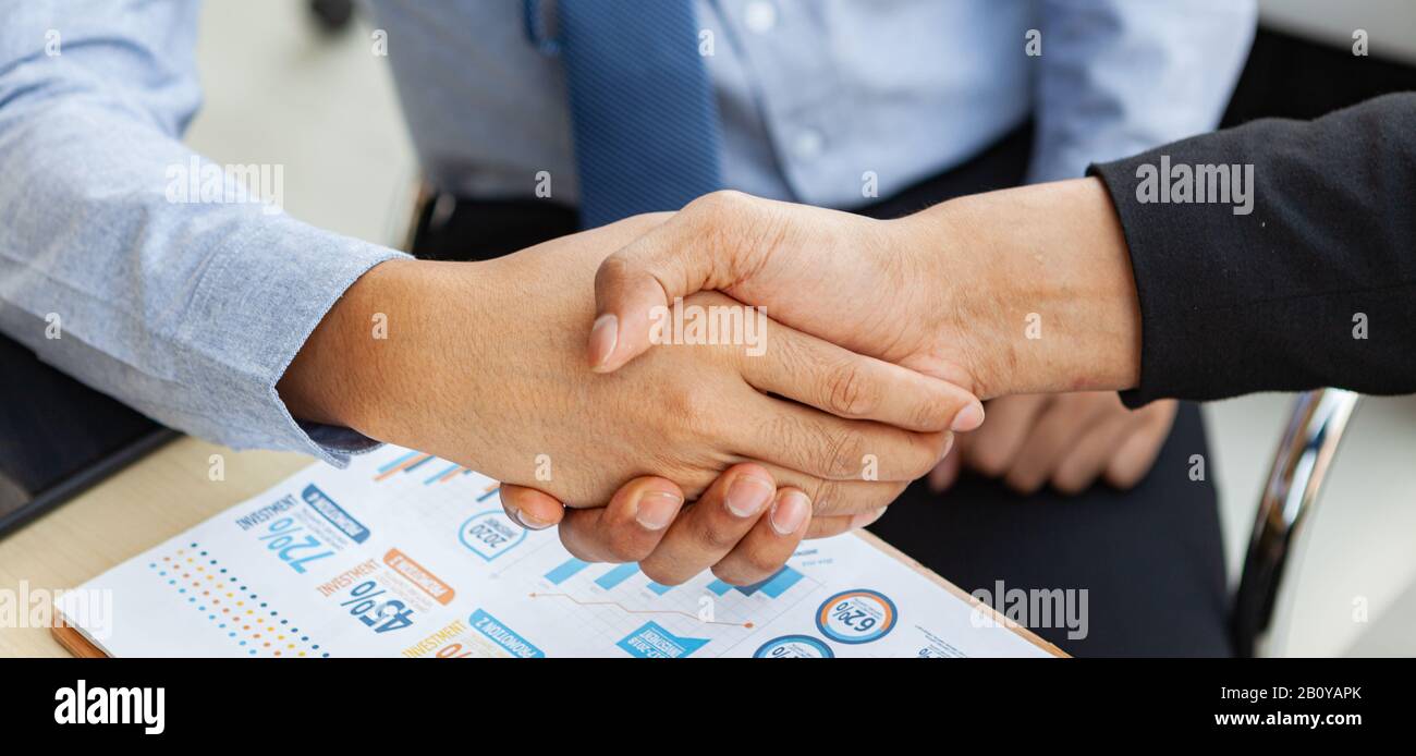 Due giovani imprenditori scuotono le mani per festeggiare il successo in ufficio con un fatturato che supera gli obiettivi aziendali. Foto Stock