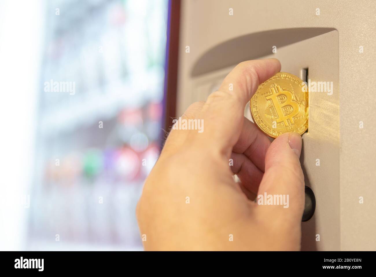 Una mano che mette un bitcoin dorato in un distributore automatico. Illuminazione interna naturale, profondità di campo bassa. Foto Stock