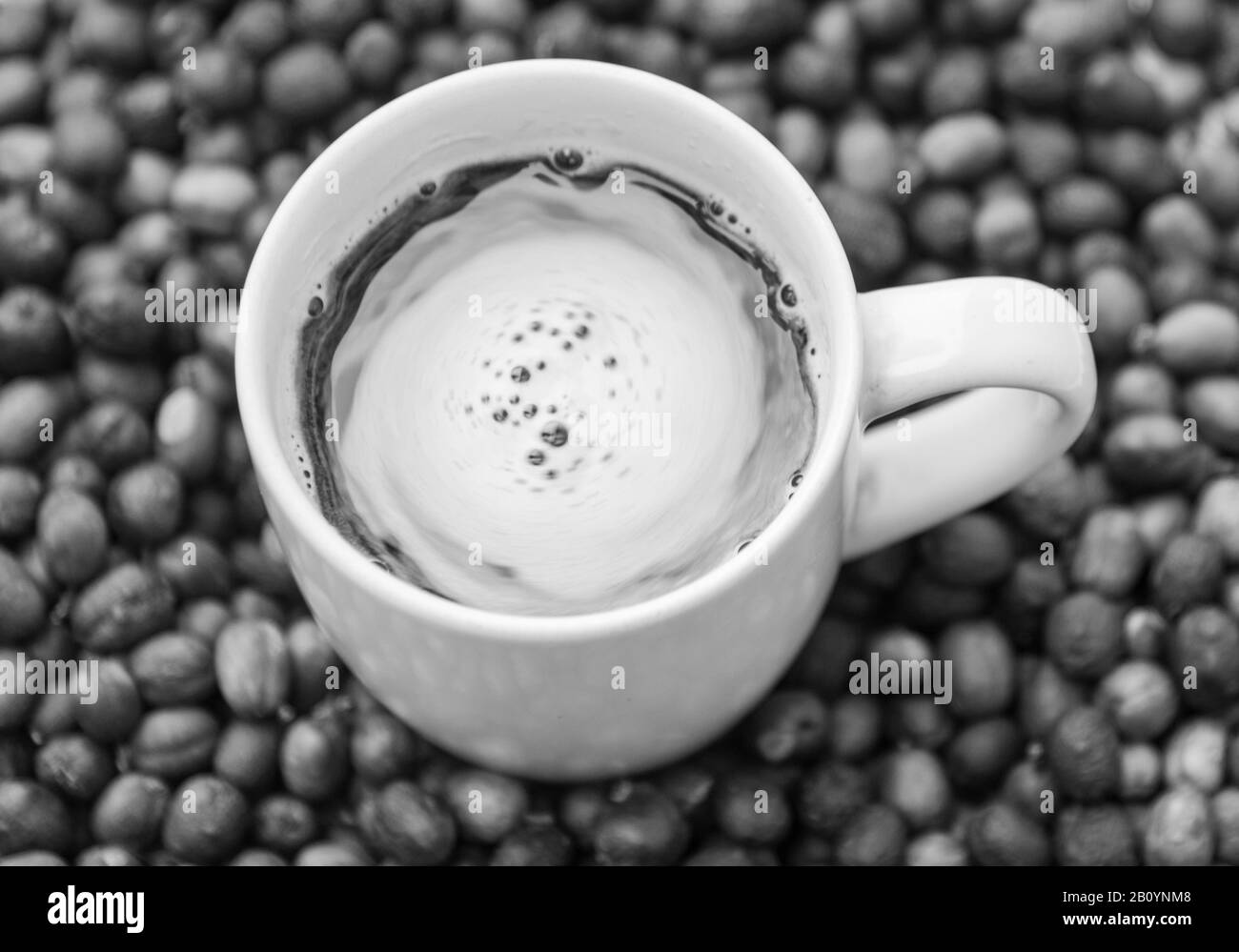 Una tazza di caffè preparato con fagioli arrostiti e macinati in modo casalingo. Espresso con panna e fagioli attorno alla tazza, spalmato su una superficie piana. Foto Stock