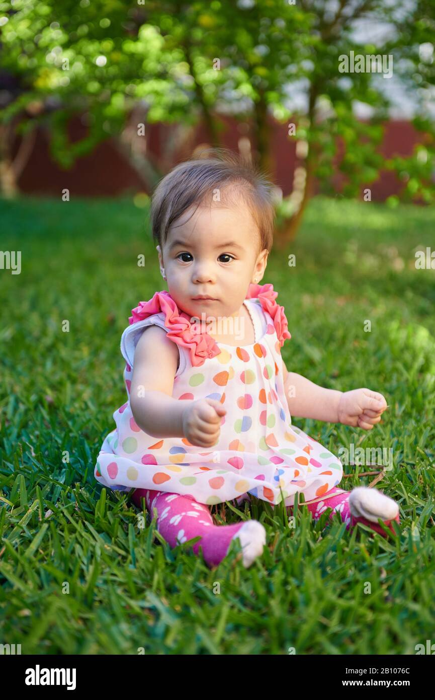 Baby ragazza seduta su erba verde in giornata di sole brillante Foto Stock