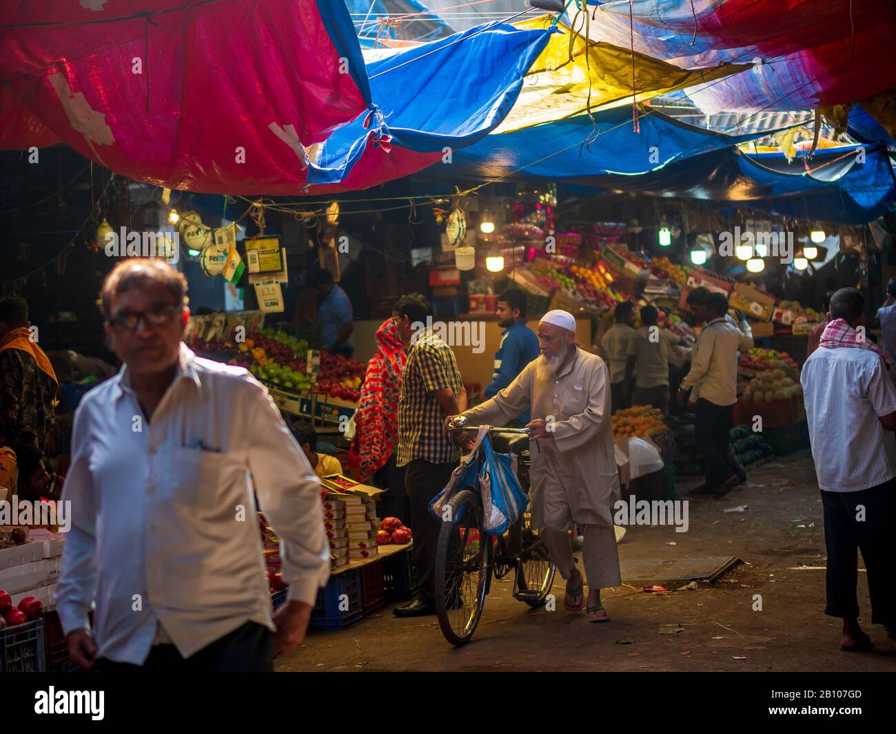 Mumbai, India - 18 dicembre 2019 : uomo musulmano di vecchia età che indossa i panni islamici tradizionali e la testa del cranio che cammina con la bicicletta in un mercato della frutta a Sout Foto Stock