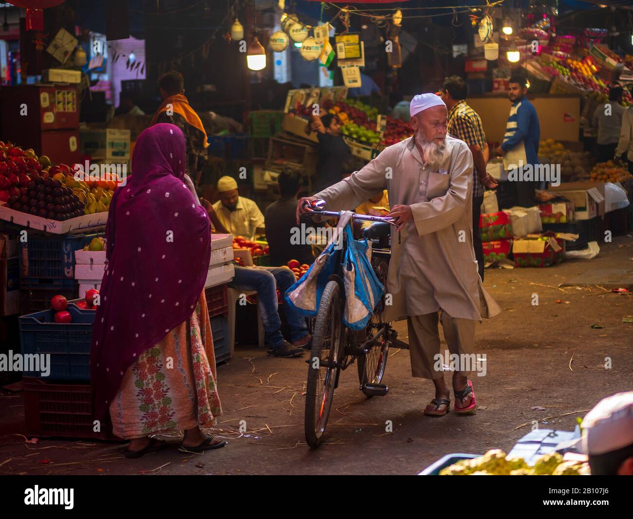Mumbai, India - 18 dicembre 2019 : uomo musulmano di vecchia età che indossa i panni islamici tradizionali e la testa del cranio che cammina con la bicicletta in un mercato della frutta a Sout Foto Stock