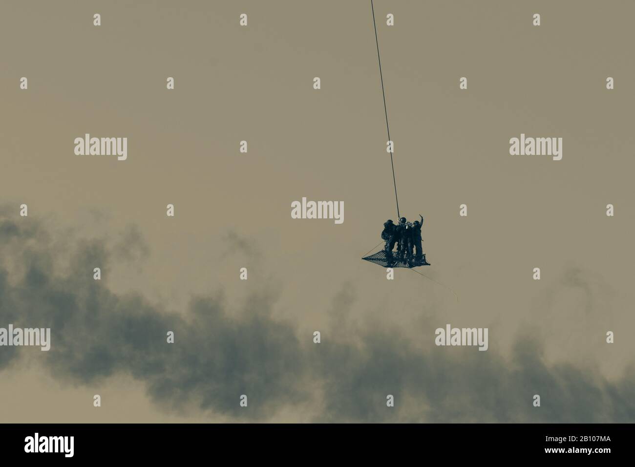 Squadra militare in conflitto resucing persone in elicottero volando attraverso l'aria su una corda collegata al trinciapaglia in fumo e haze in Medio Oriente Foto Stock